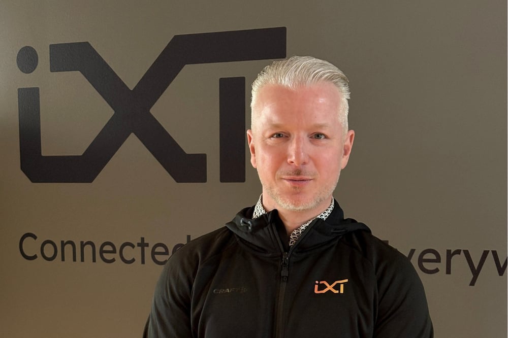 Jelger Smit in a black hooded jacket with IXT logo on. IXT logo in black on the wall behind him. 